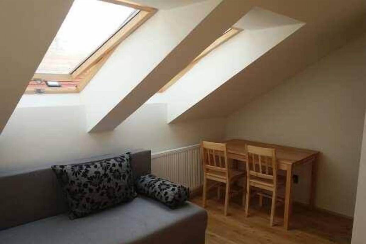 A small, cozy room with a sloped ceiling and skylights, a gray sofa with patterned cushions, and a wooden table.