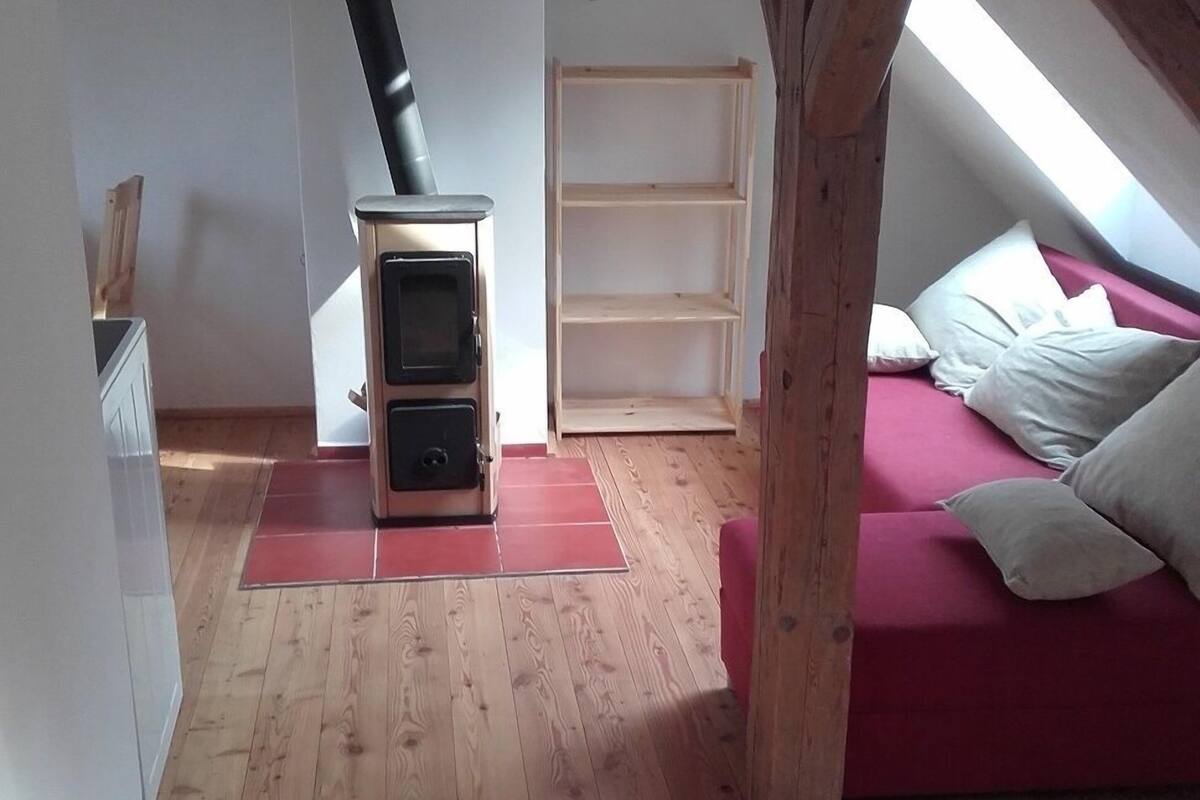 A loft bedroom with a wooden floor, a red sofa, a white bed, and a wood-burning stove.