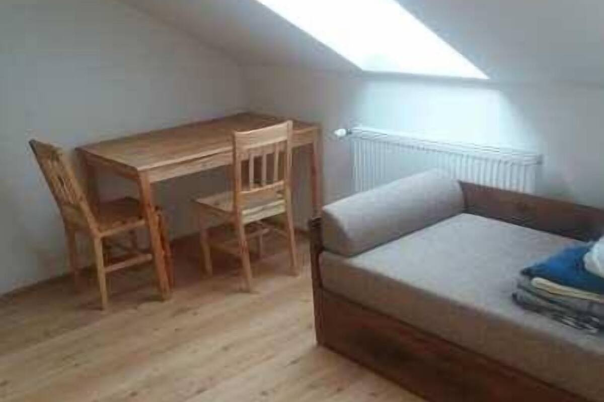 A small, open-plan room with a wooden dining table and chairs, a sofa, and a skylight.