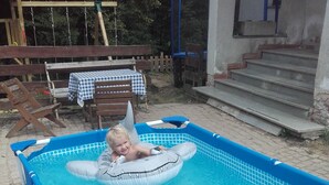A small inflatable pool with a child floating inside, surrounded by a grassy area and a wooden deck with a table and chairs. - Kyprův mlýn (Knínice)