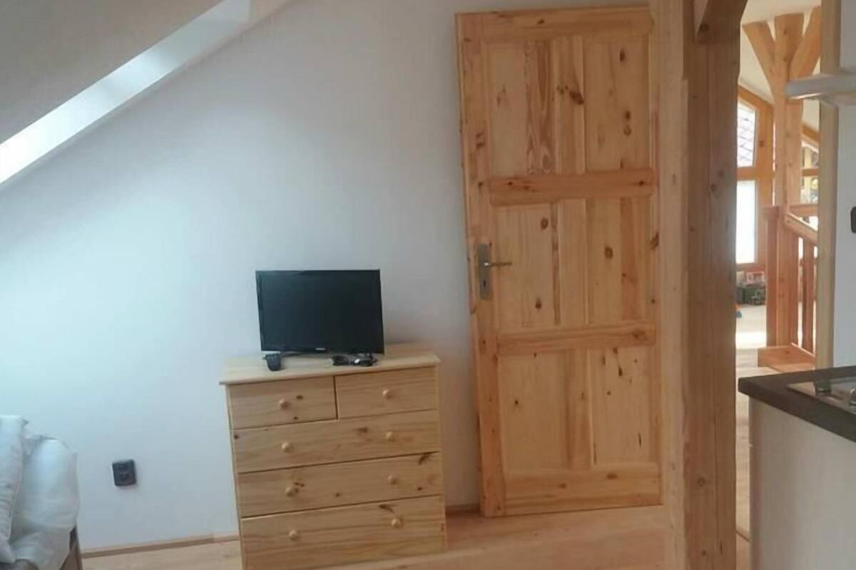 A room with a sloped ceiling, wooden flooring, a TV on a dresser, and a wooden door.