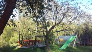 A playground with a slide, a swing set, and a picnic table in a grassy area with trees. - Kyprův mlýn (Knínice)