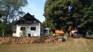 A two-story house with a sloped roof, a stone wall in front, and a wooden deck. - Kyprův mlýn (Knínice)