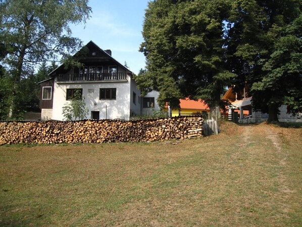 Une maison à deux étages, avec un toit en pente, un mur en pierre à l’avant et une terrasse en bois.