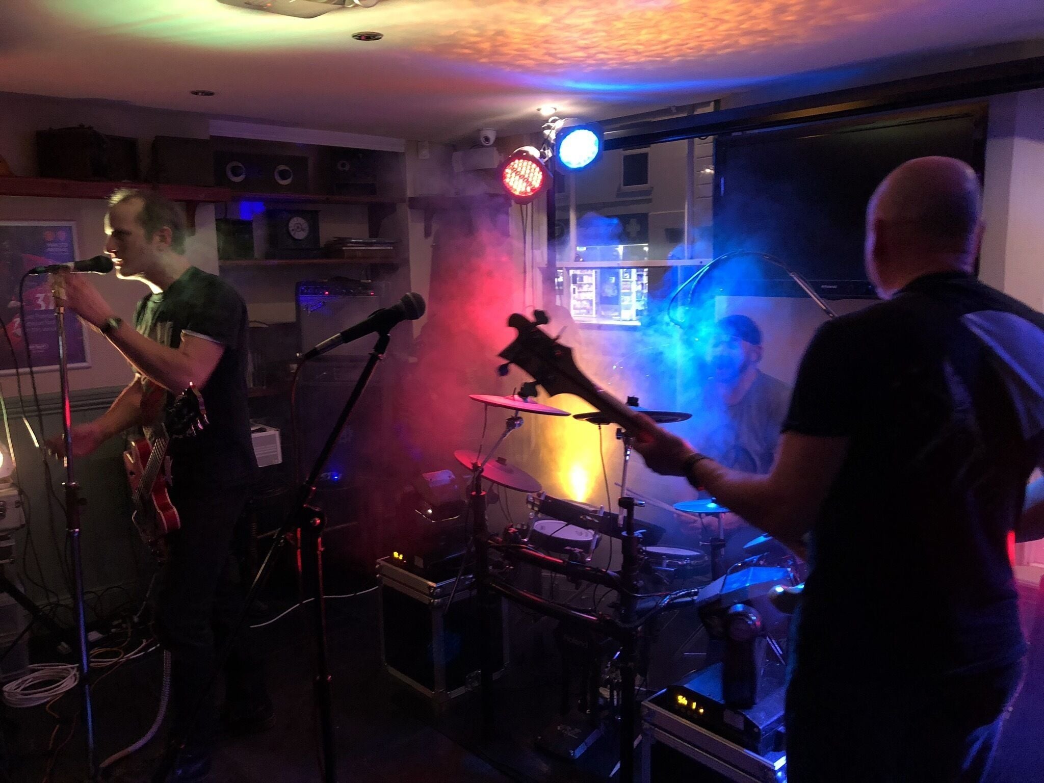 A band performing in a dimly lit room with a drum set and musical equipment.