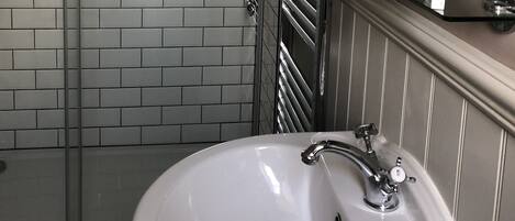 A bathroom with a white sink, a glass shower enclosure, and a mirror with toiletries.