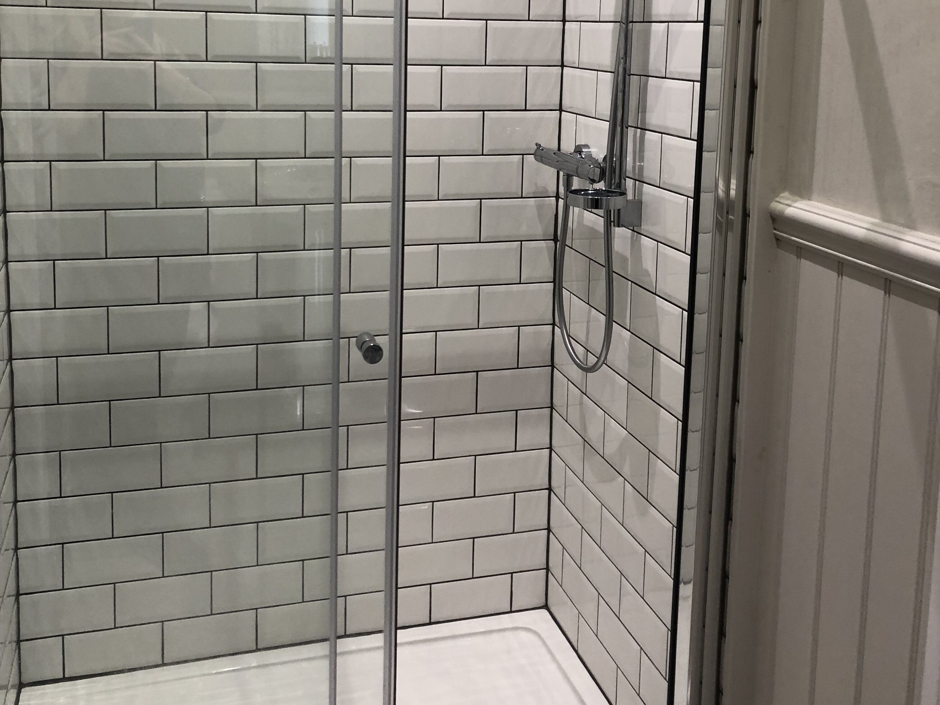 A shower with a glass door and white tiled walls.