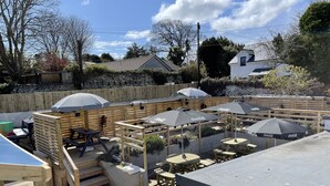 Ein Terrassenbereich im Freien mit Holztischen und -bänken, umgeben von Steinmauern und Holzzäunen.