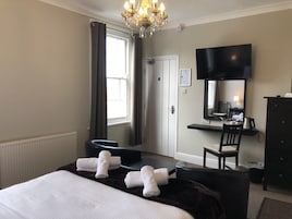Una habitación de hotel con cama, escritorio, silla, televisor y cómoda.