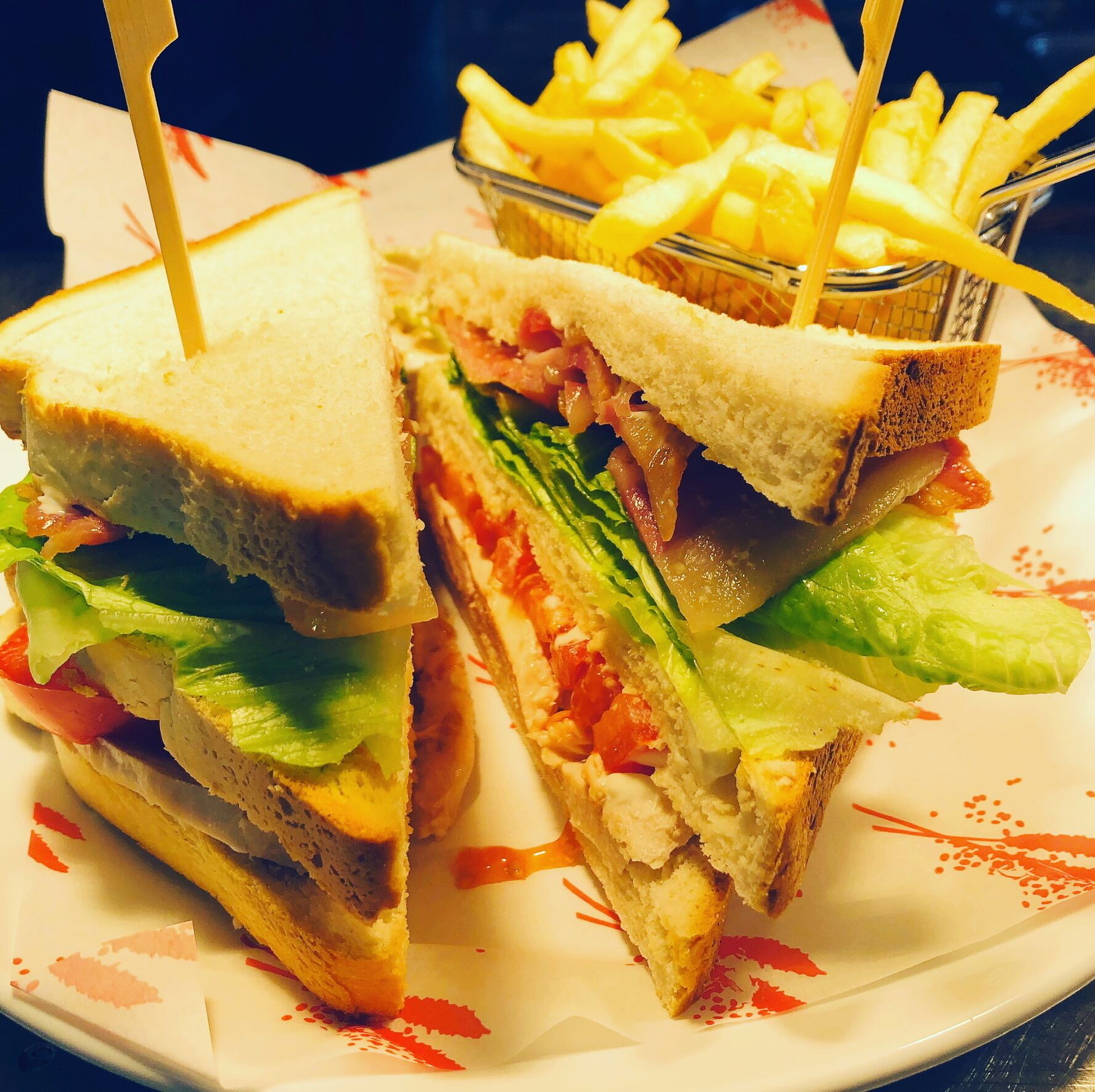 A sandwich cut in half with lettuce, tomato, and other fillings, served on a plate with a side of French fries.