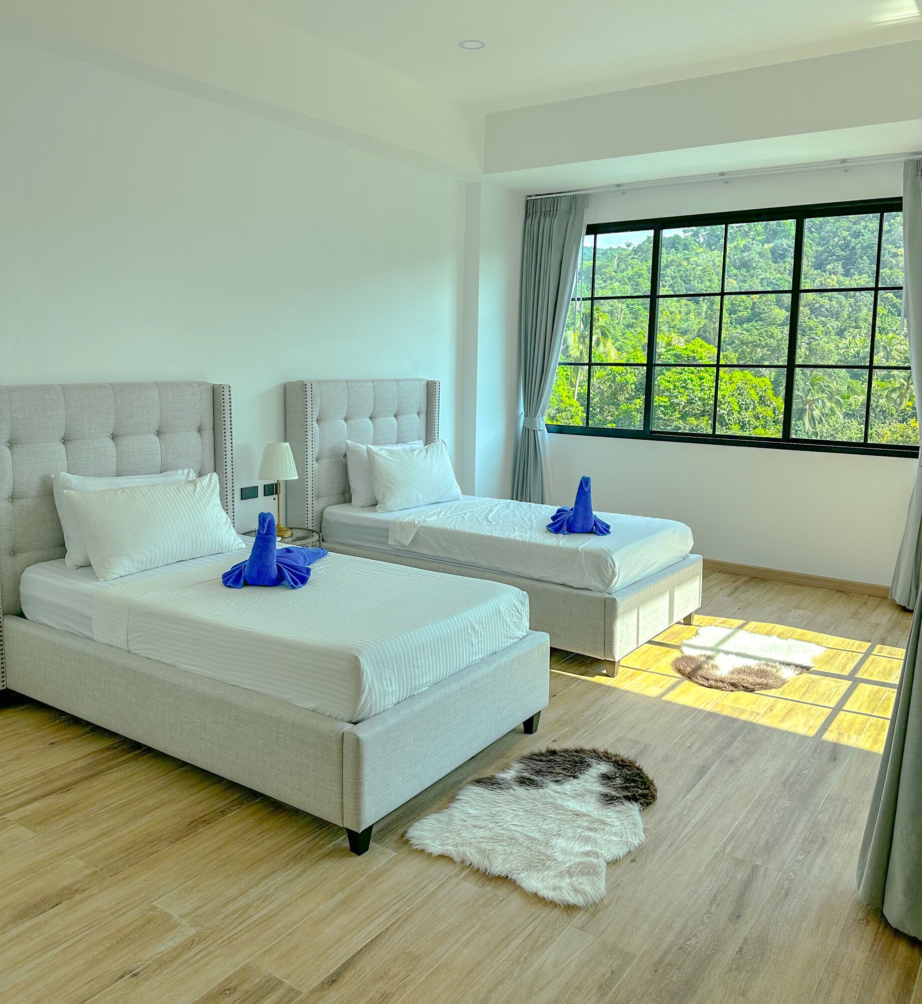 Ein modernes Schlafzimmer mit zwei Betten, einem großen Fenster und Blick auf Grünflächen sowie Holzdielen.