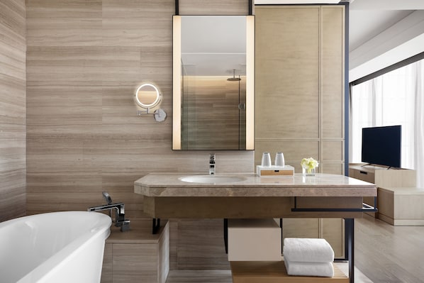 A modern bathroom with a freestanding bathtub, a large mirror, a vanity with a sink, and a television.