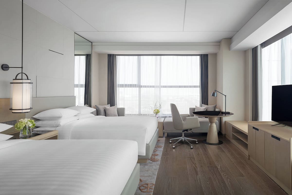 Une chambre d’hôtel avec deux lits, un bureau, une chaise, une télévision et de grandes fenêtres.