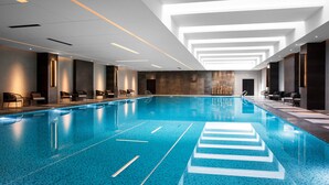 A modern indoor swimming pool with clear lane markings, recessed lighting, and contemporary furniture.