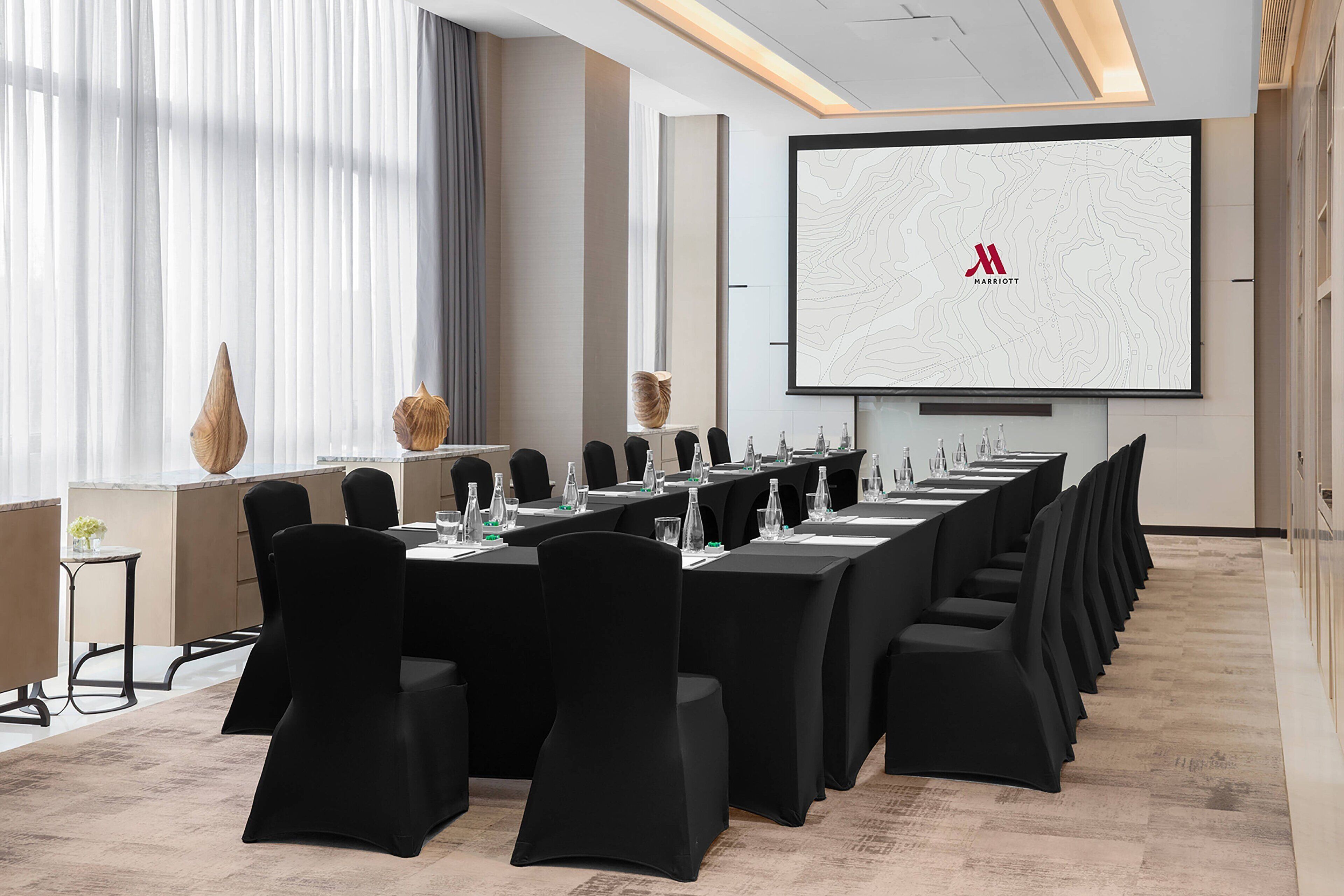 A conference room with a long table, black chairs, and a large screen displaying a logo.
