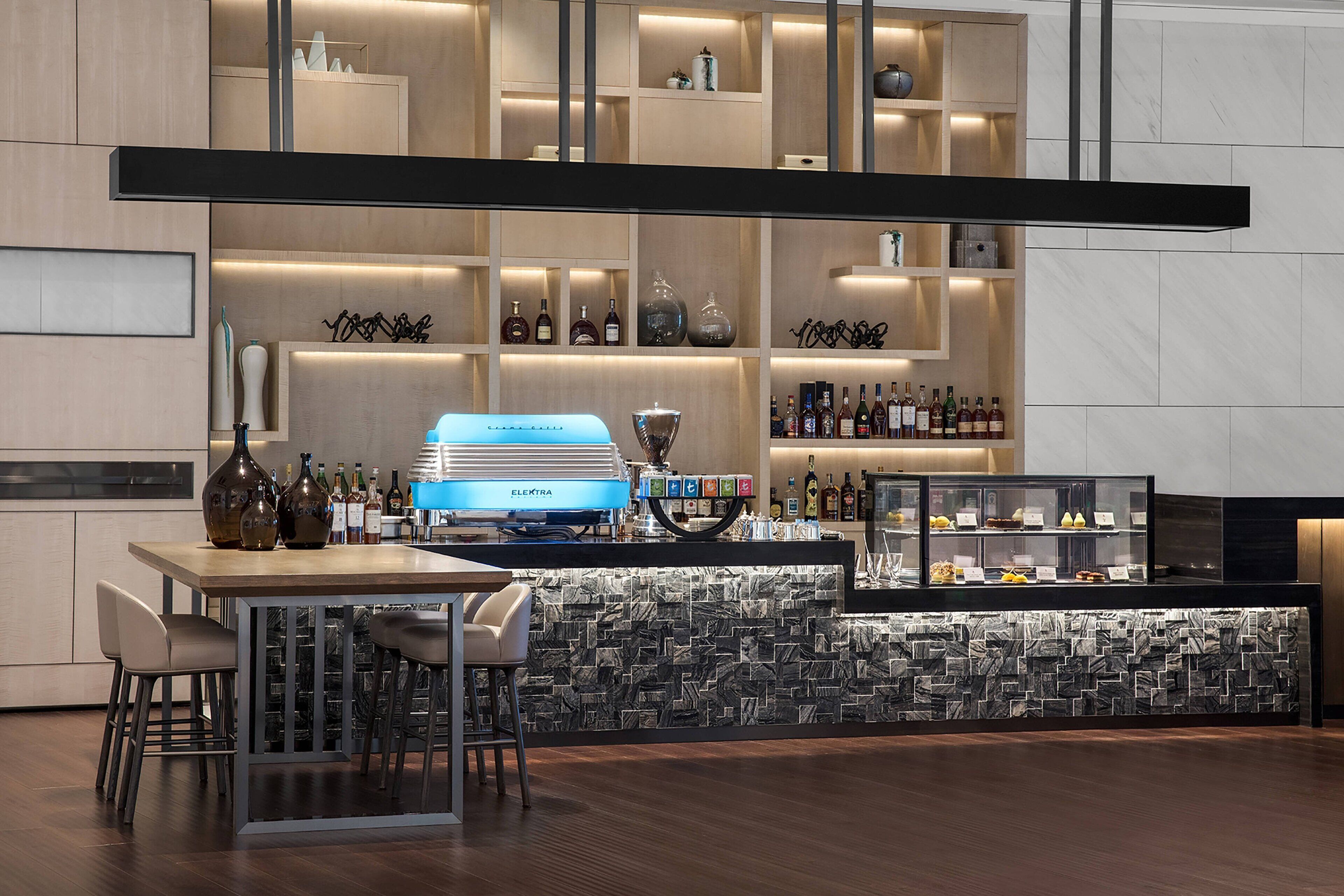 A modern bar area with a counter, seating, and shelves of bottles.