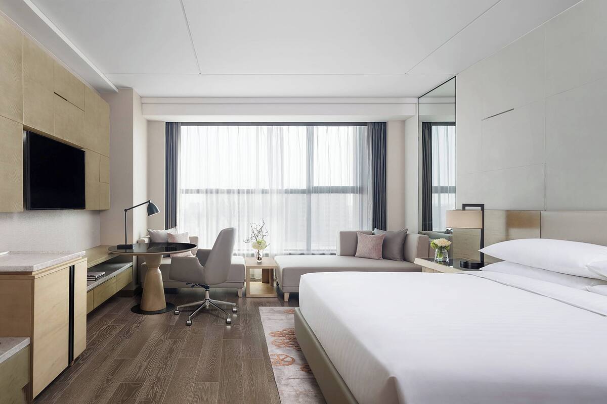 Une chambre d’hôtel avec un lit, un bureau, une chaise, une télévision et une grande fenêtre.