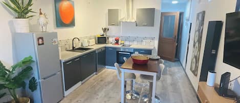A compact kitchen with modern appliances, a dining area with a small table and chairs, and a red sofa in the foreground.