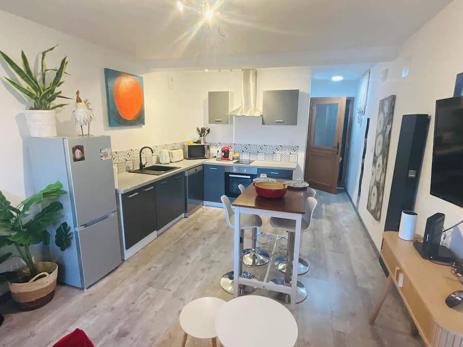 Une cuisine compacte dotée d’appareils électroménagers modernes, un coin repas avec une petite table et des chaises, et un canapé rouge en premier plan.