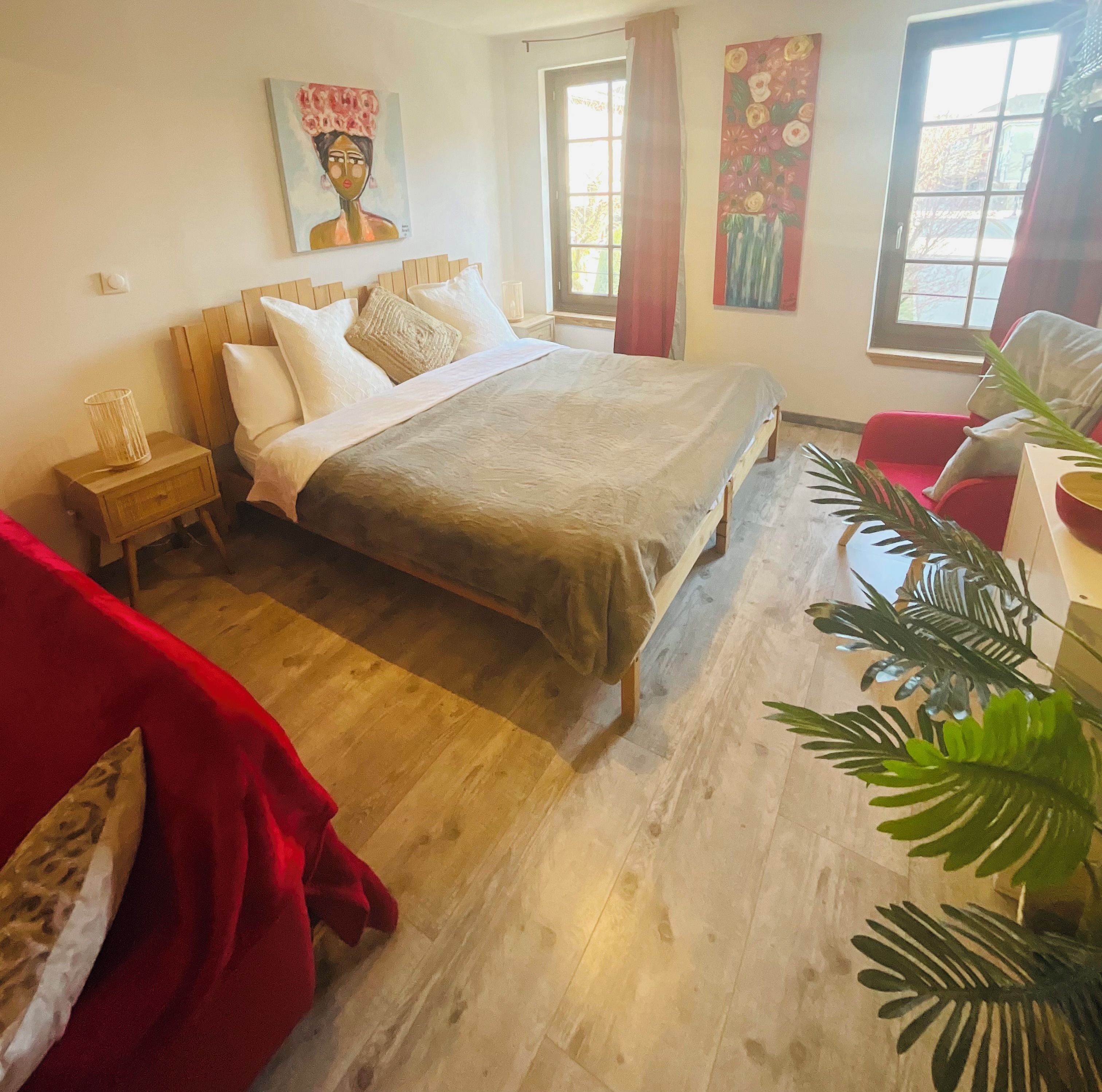Un dormitorio con cama de madera, una mesita de noche, una silla roja y una ventana con cortinas.