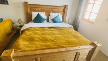 Una cama de madera con un edredón amarillo, dos almohadas y una mesita de noche con una lámpara.