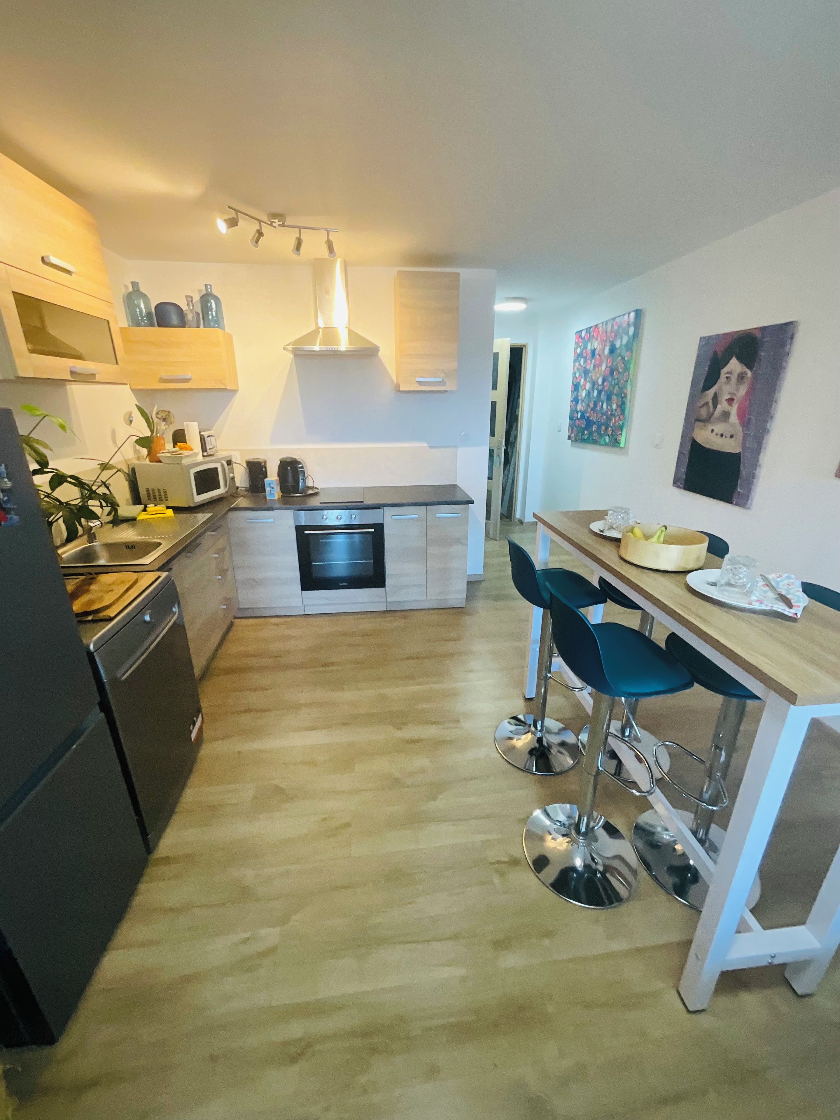 Una cocina moderna con horno integrado, microondas y fregadero. Hay taburetes de bar y una mesa de comedor con un florero.