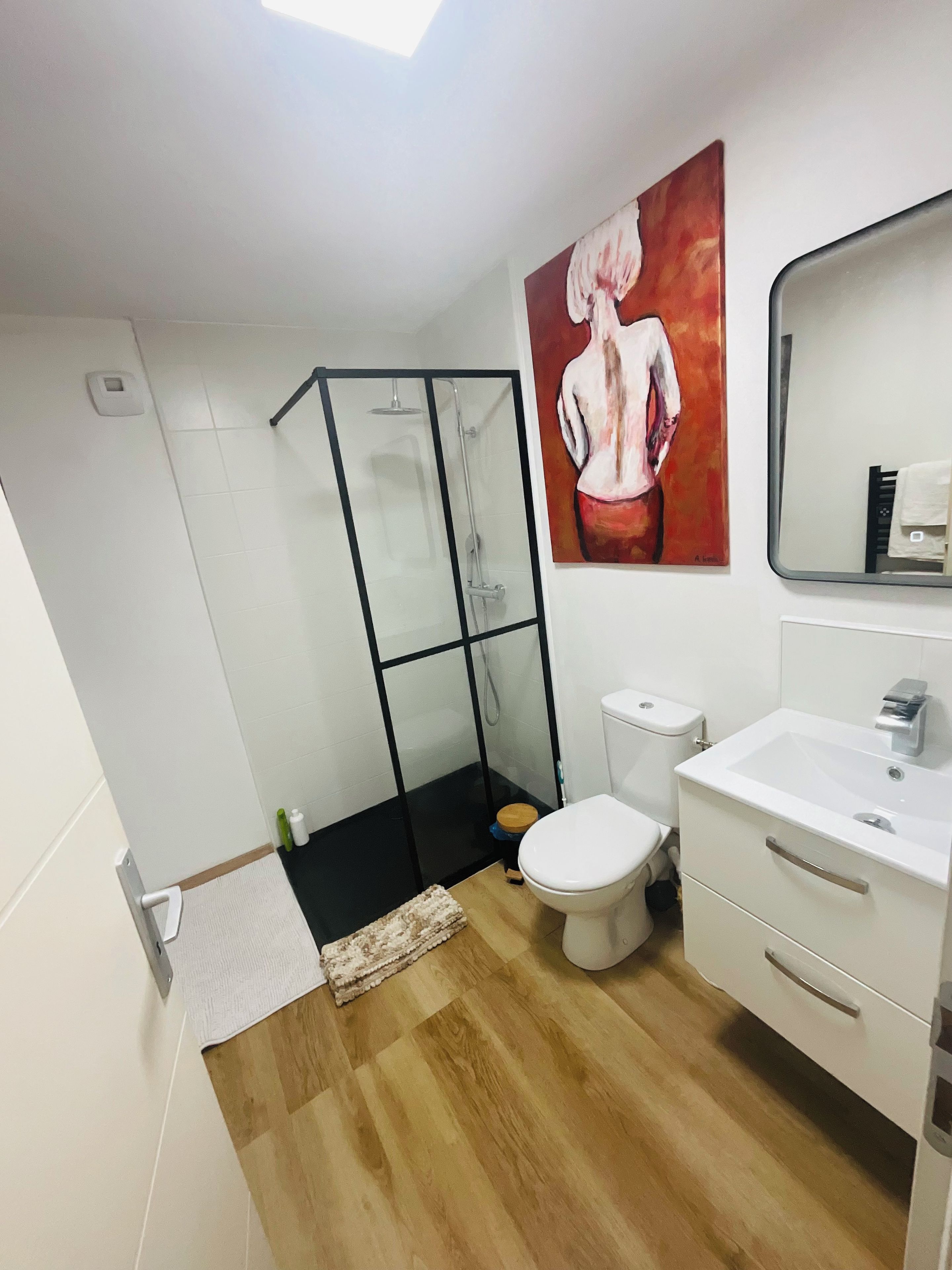 Un baño moderno con cabina de ducha de vidrio, inodoro blanco y lavabo con espejo sobre él.