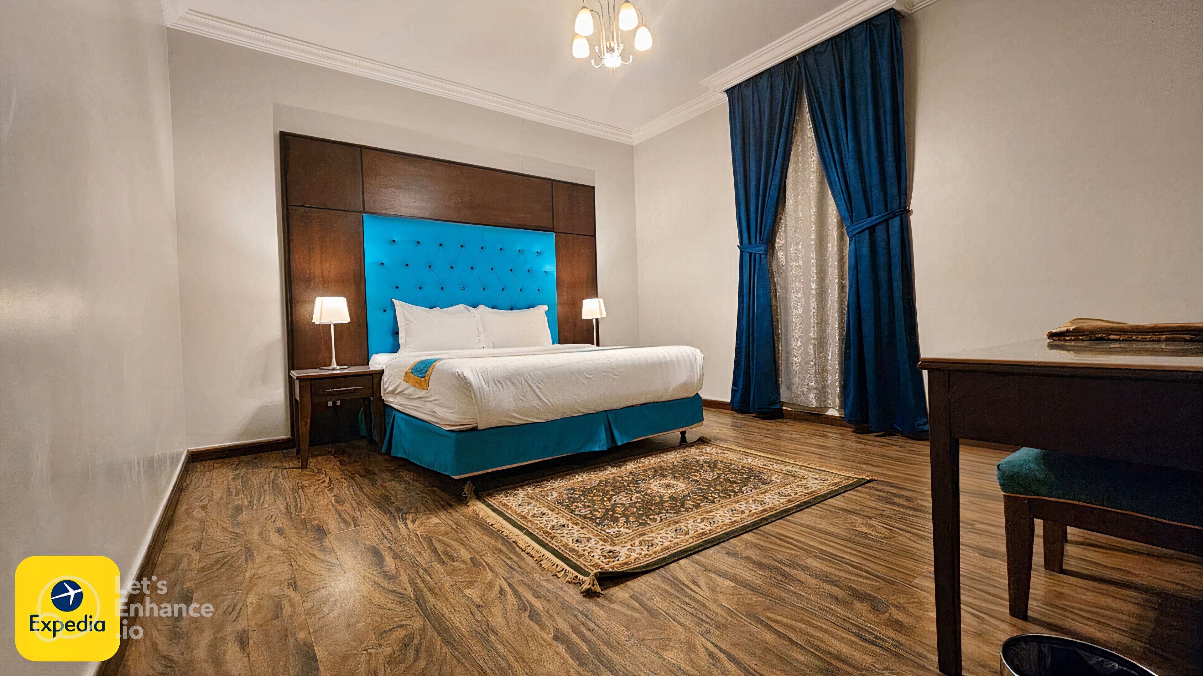 A hotel room with a large bed, a wooden floor, a desk, and a chandelier.
