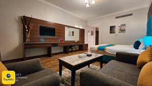 Une chambre d’hôtel avec un bureau en bois, un lit recouvert d’une courtepointe bleue et jaune, une télévision et un coin salon avec deux canapés.