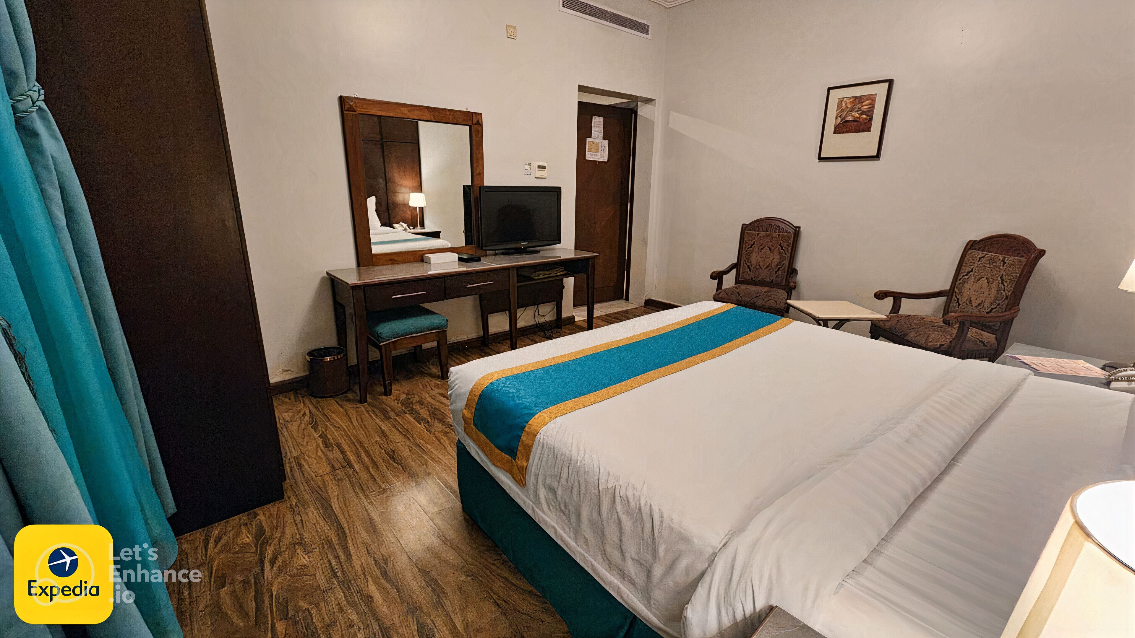 A hotel room with a bed, a desk, a television, and two chairs.