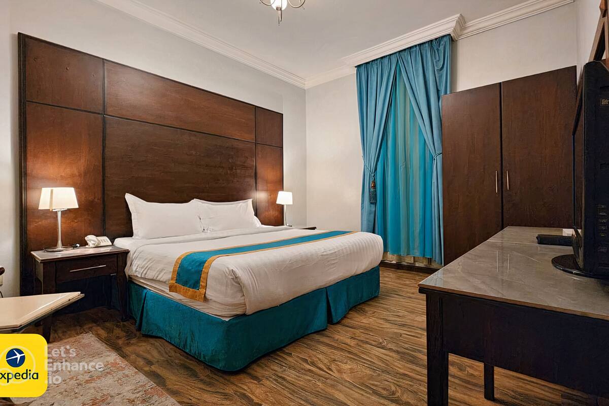 A hotel room with a large bed, two bedside lamps, a desk with a television, and a blue curtain.