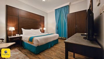 A hotel room with a large bed, two bedside lamps, a desk with a television, and a blue curtain.