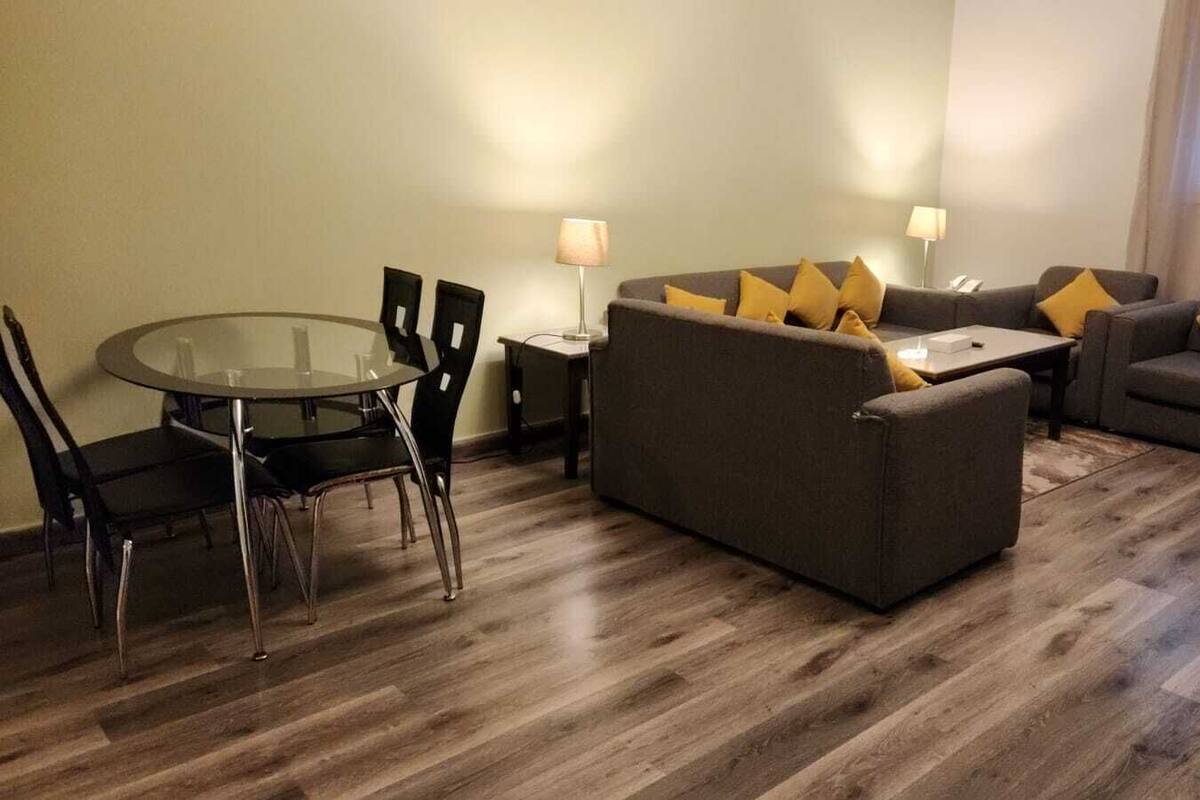 A modern living room with a glass dining table, two sofas with yellow cushions, and a wooden floor.