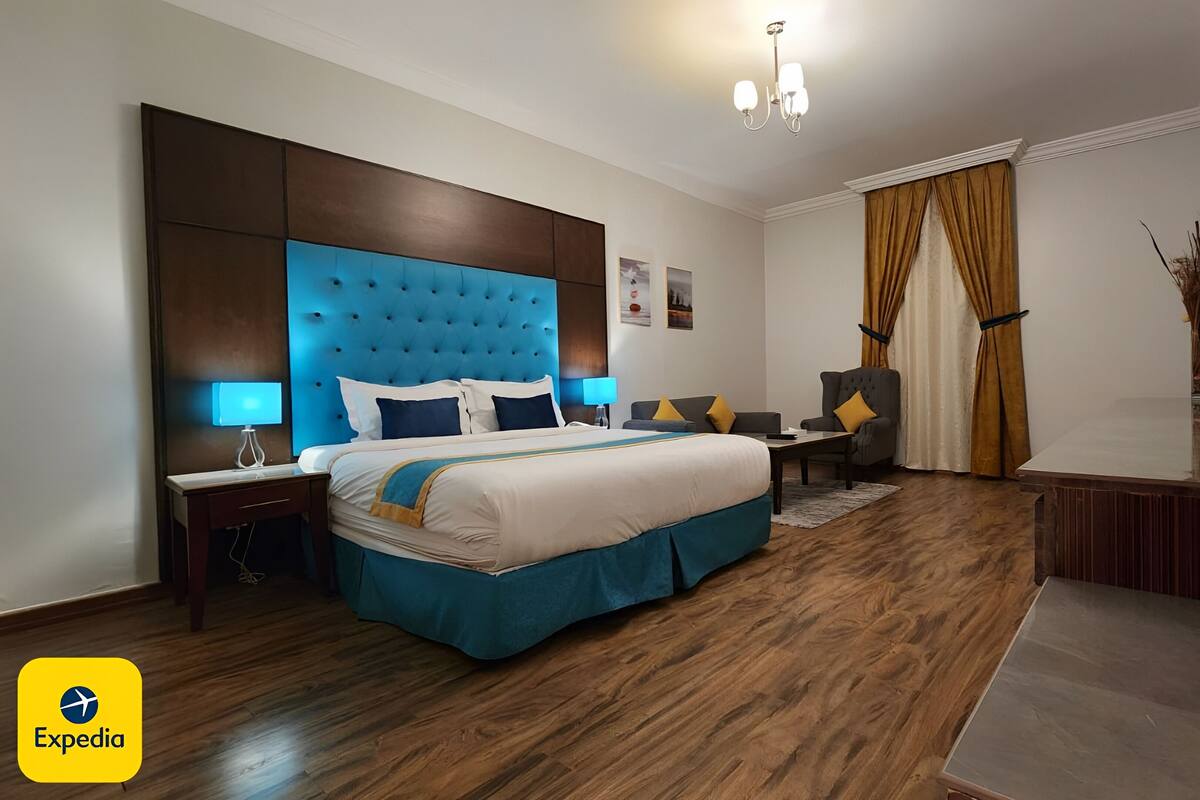 A hotel room with a large bed, a desk, a chair, and a mirror.