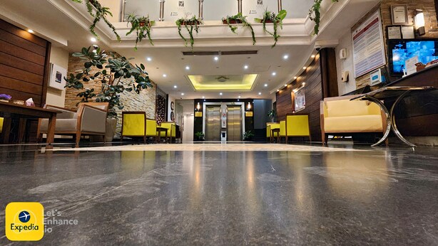 Un hall d’hôtel avec un sol en marbre, des chaises jaunes, un comptoir d’accueil et des plantes suspendues.