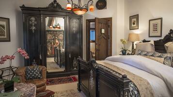 A bedroom with a large bed, a dark wooden wardrobe, a mirror, and a small table with a plant.