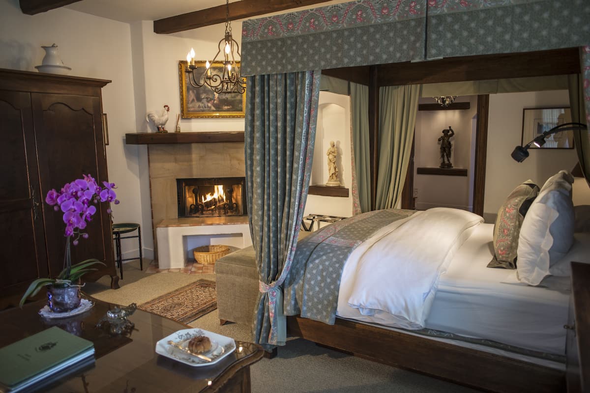 A bedroom with a four-poster bed, a fireplace, and a chandelier.
