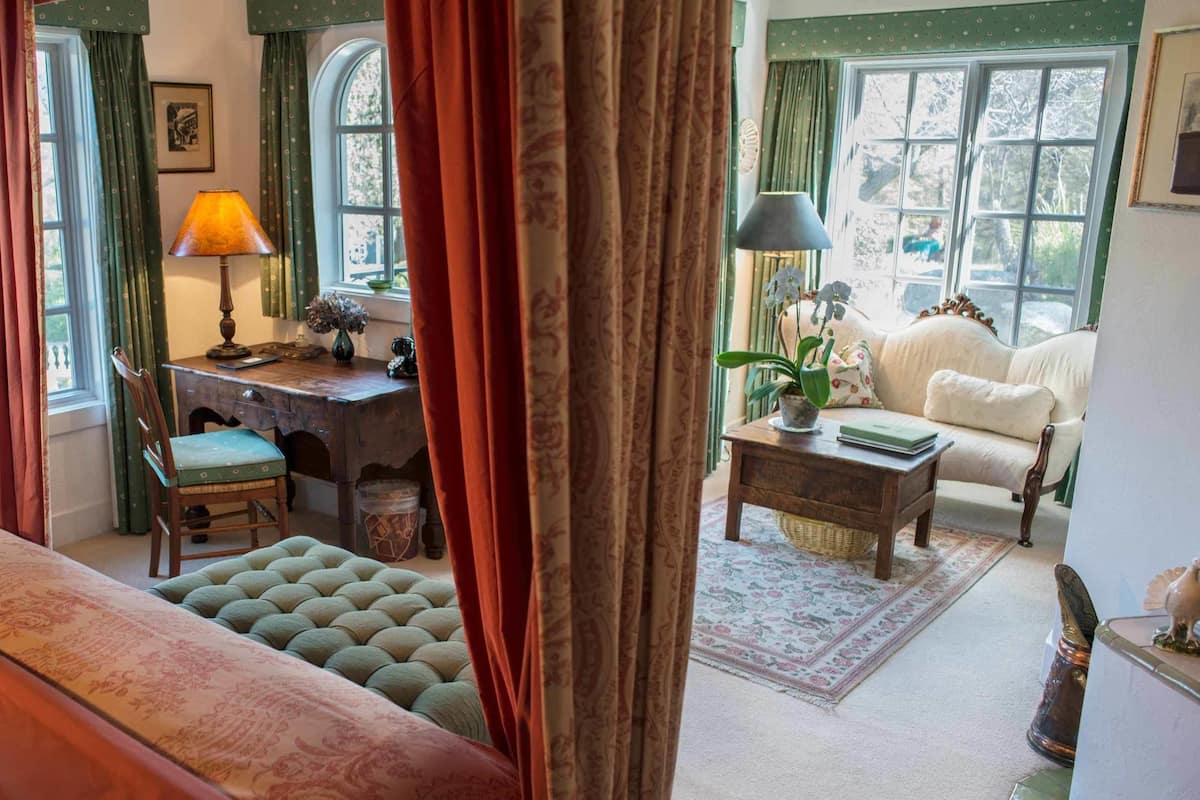 A cozy room with a bed, a desk, a chair, a sofa, and a window with curtains.