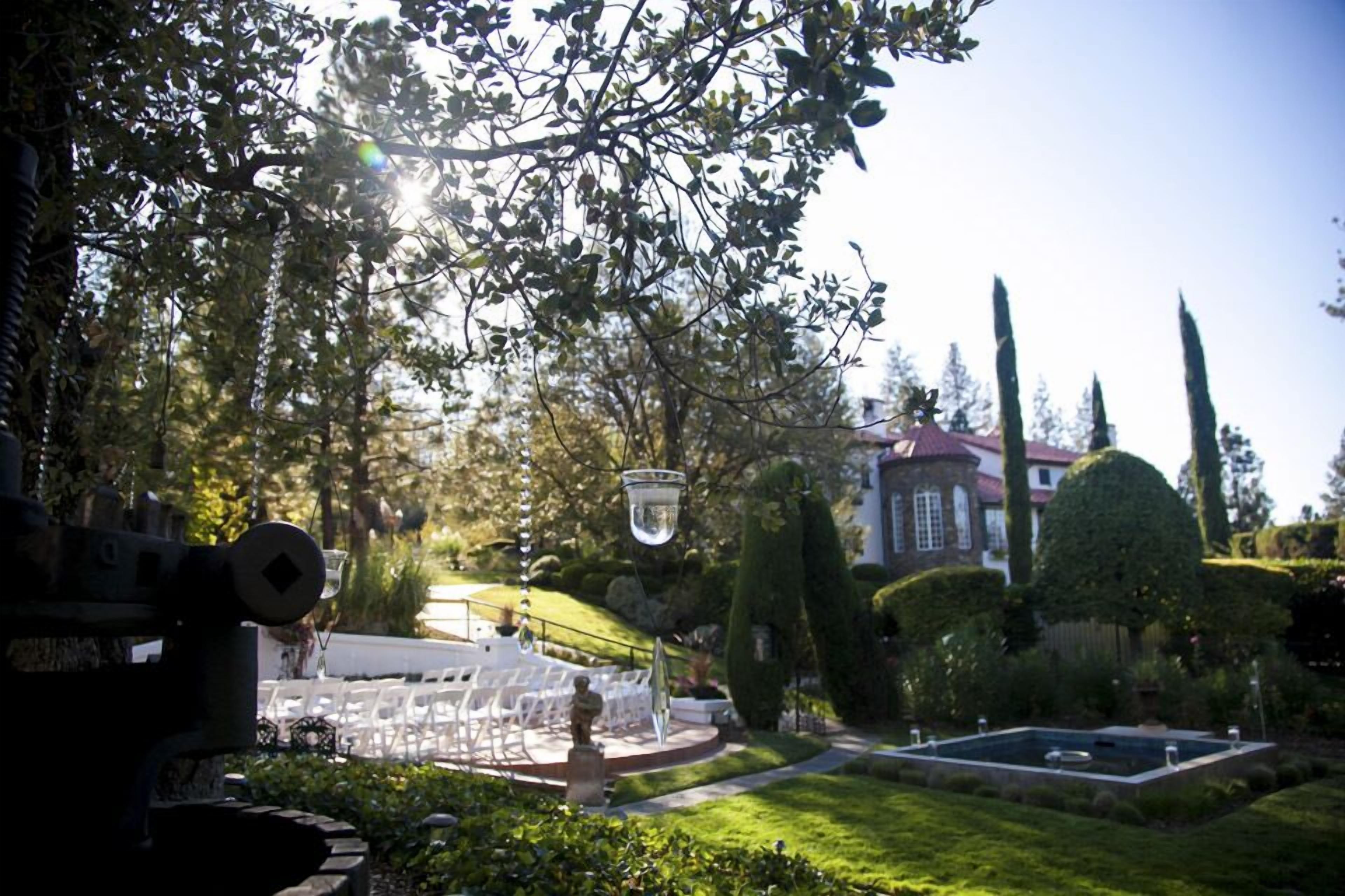A garden with a fountain, neatly trimmed hedges, and a building in the background.