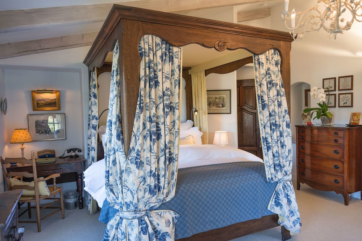 A bedroom with a four-poster bed, wooden furniture, and a chandelier.