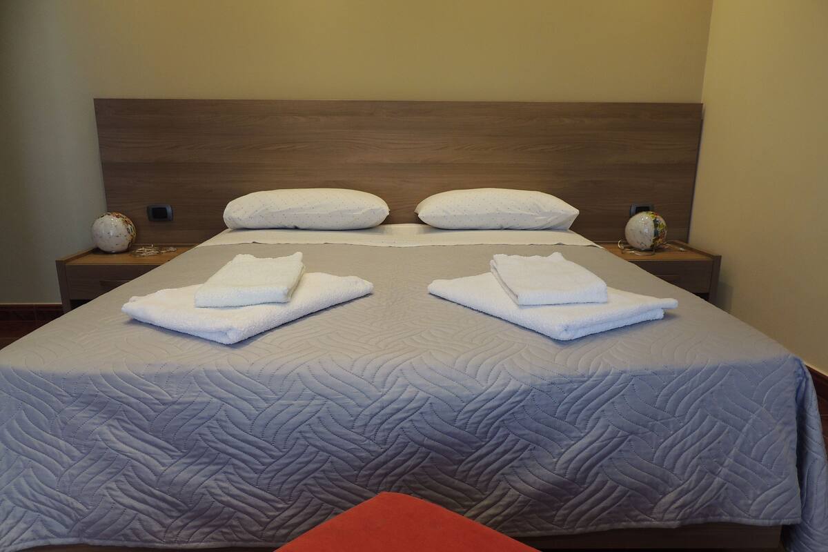 Una cama bien hecha con un cabecero acolchado, dos almohadas y toallas dobladas sobre la cama.