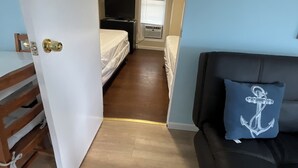 Ein gemütlicher Raum mit Bett, Schreibtisch, schwarzem Schlafsofa und einem Fenster mit Jalousien.
