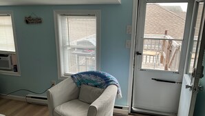 Ein Zimmer mit einem weißen Sessel, einer Tür mit Blick ins Freie und einer Wand-Klimaanlage.