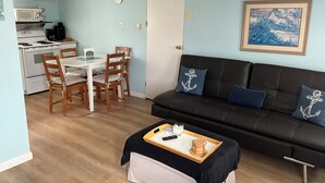 Ein kompakter Wohnraum mit Küchenzeile, einem Essbereich mit Stühlen, einer Couch mit Kissen und einem Bild an der Wand.