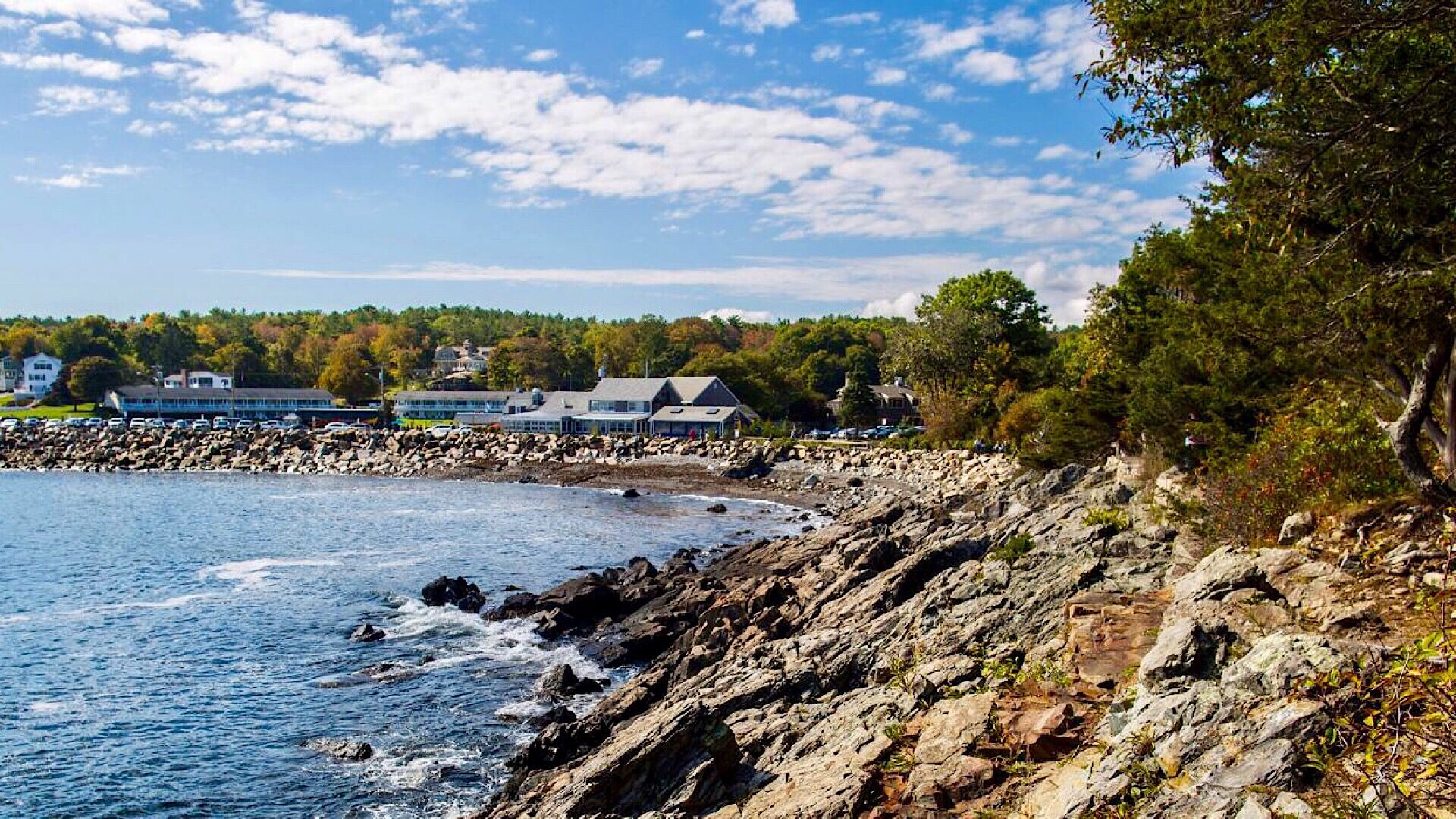 A coastal hotel with a rocky shoreline, a view of the sea, and buildings in the background.
