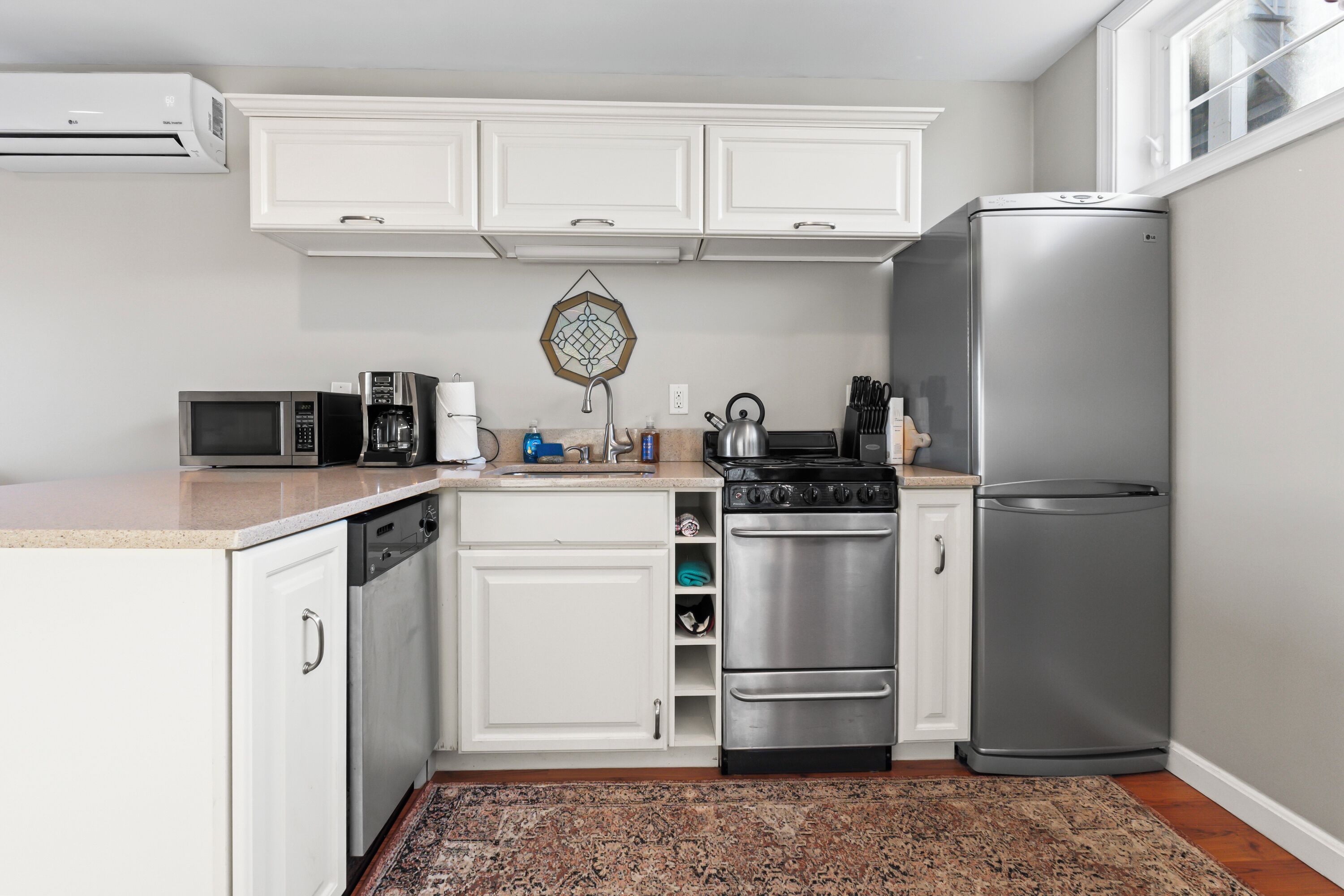 A compact kitchen with white cabinets, a stainless steel refrigerator, a microwave, a kettle, and a dishwasher.