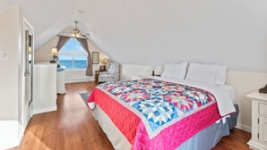 Ein Schlafzimmer mit einem großen Bett, einem Deckenventilator, einem Fenster mit Vorhängen und Blick aufs Meer.