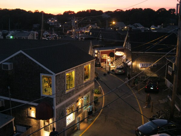 A street view at dusk with buildings, a visible storefront, and a car parked on the side.