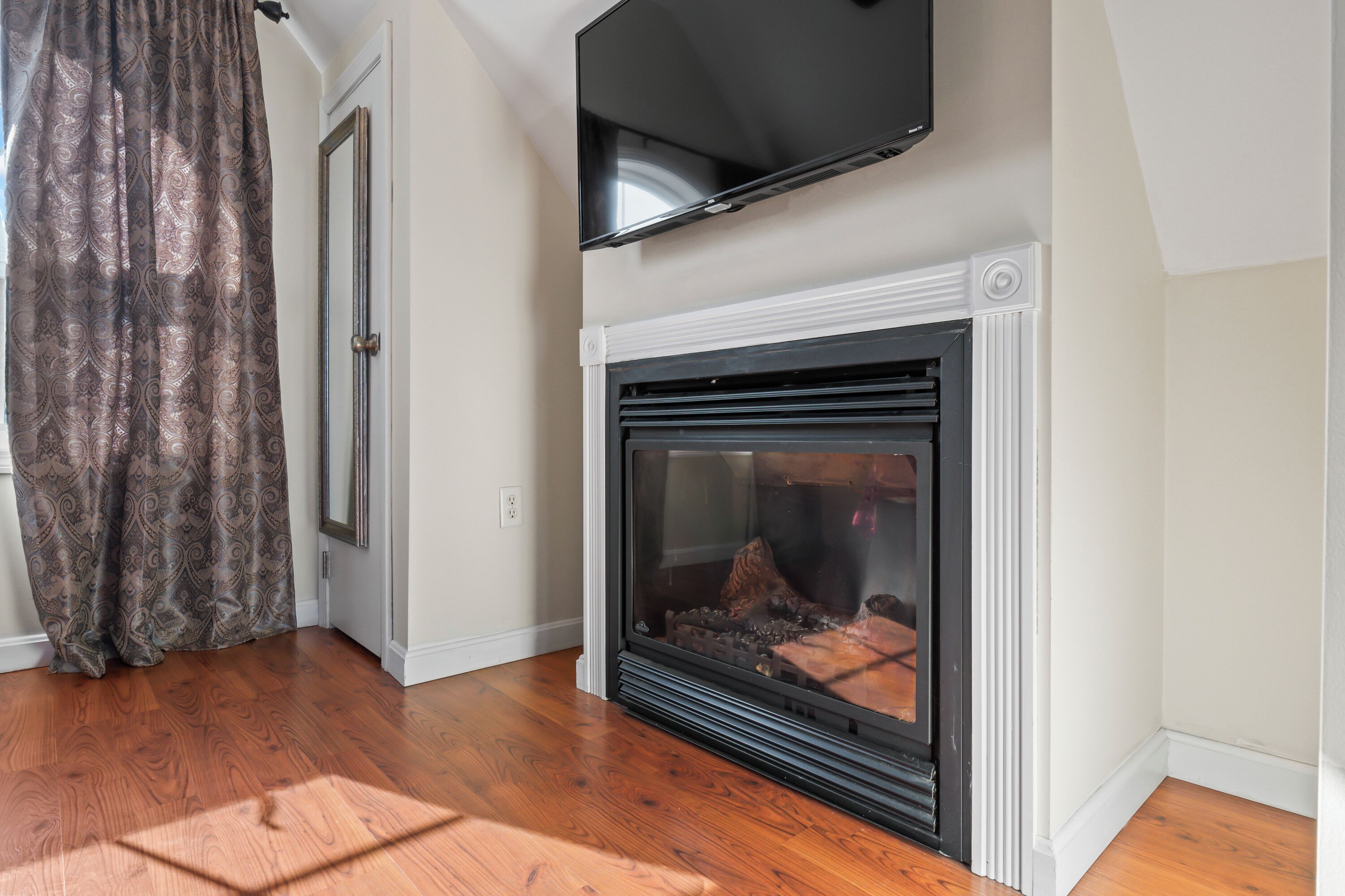 A room with a fireplace, a television mounted above it, and a patterned curtain.