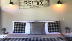A bedroom with a bed, checkered bedding, a 'RELAX' sign, two wall-mounted lamps, and a wooden ceiling. - Cozy Mountain Log Cabin With Amazing Views!  (Pine)